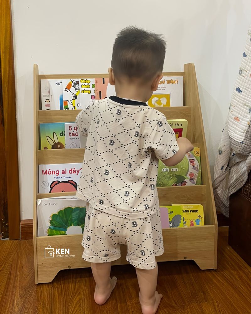 Bé đứng trước kệ sách 4 tầng, tự chọn sách trên tầng vừa tầm tay