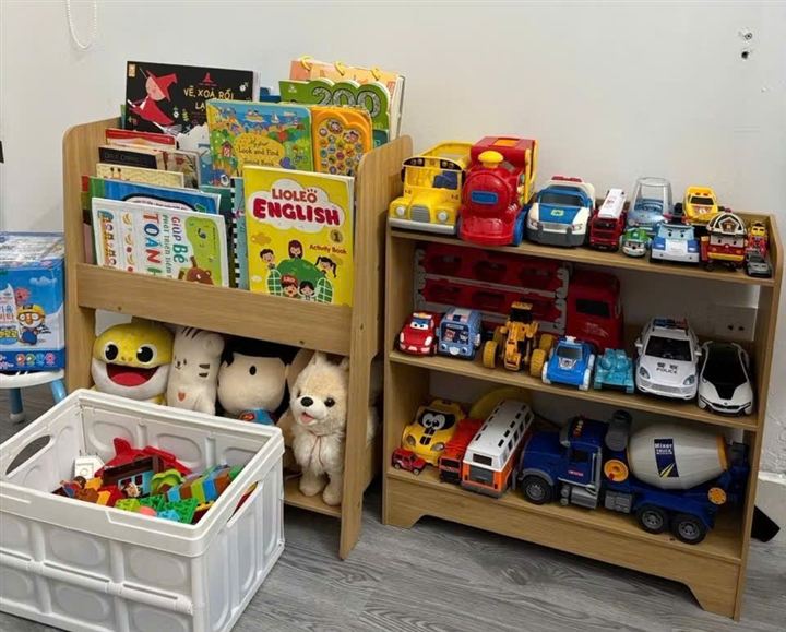 Kệ sách và kệ đồ chơi xếp cạnh nhau, đầy sách và xe đồ chơi